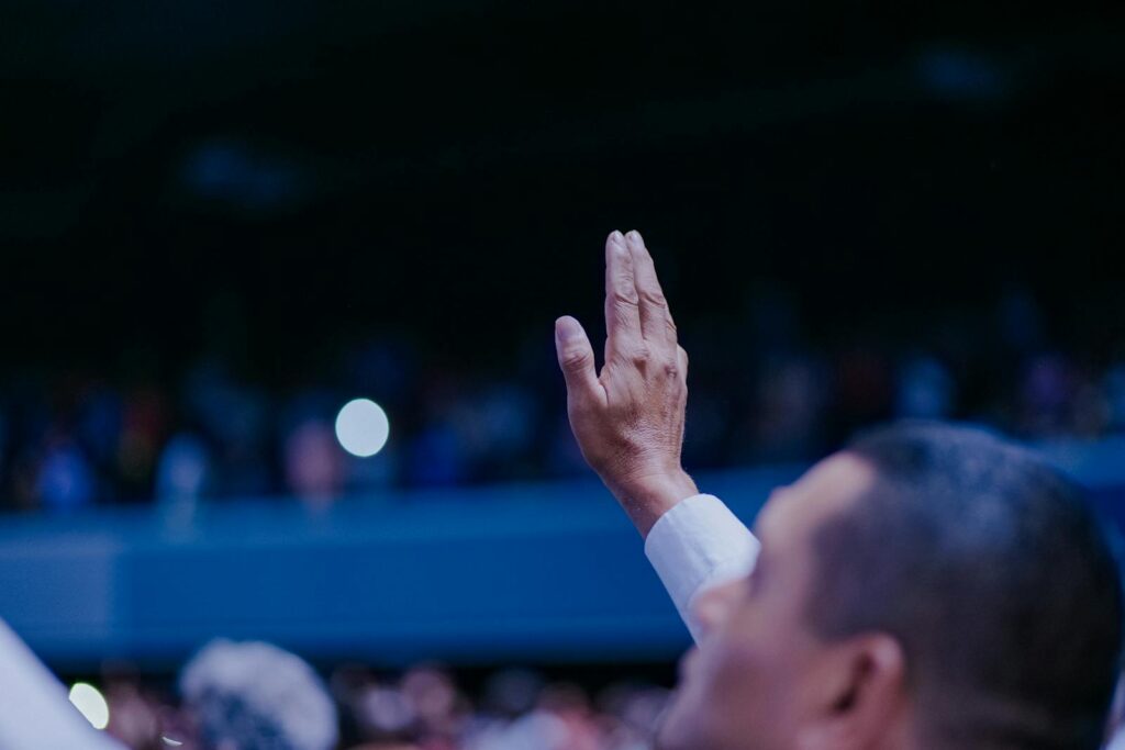 A close-up of a raised hand in a crowded public gathering, symbolizing engagement.